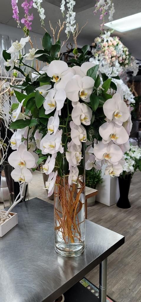 A vase filled with white orchids is sitting on a table.