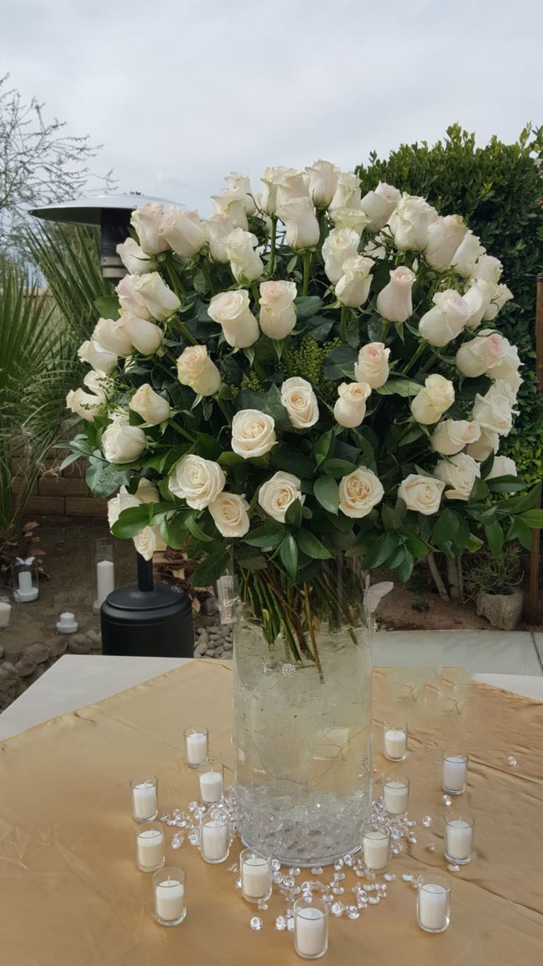 A vase filled with white roses and candles on a table.