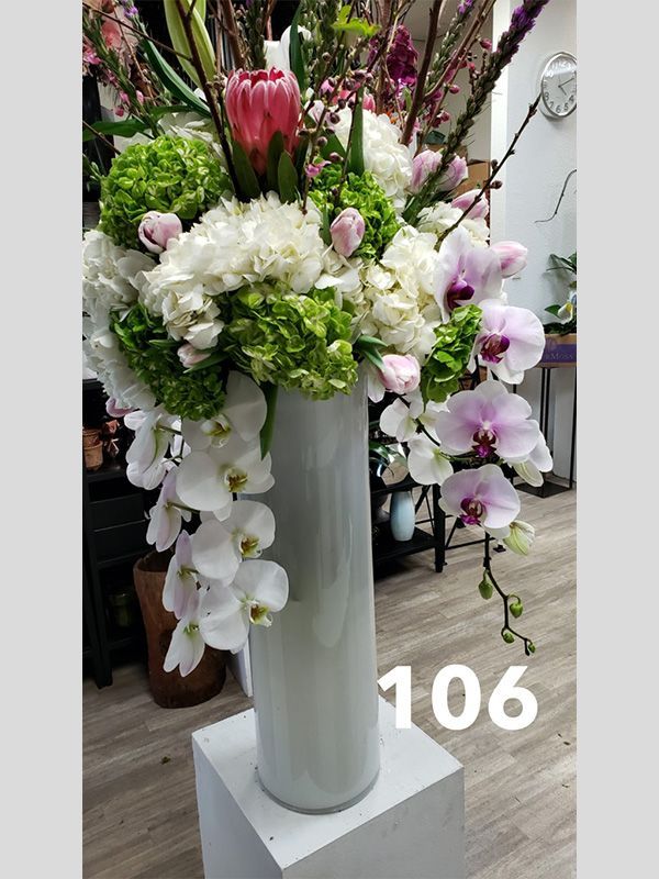 A white vase filled with flowers is sitting on a pedestal.