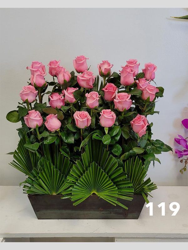 A vase filled with pink roses and green leaves on a table.