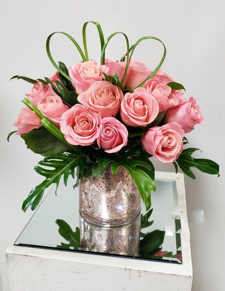 A vase filled with pink roses is sitting on a mirrored table.