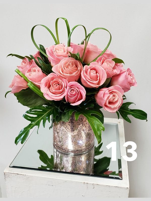 A vase filled with pink roses is on a table with the number 13 on it