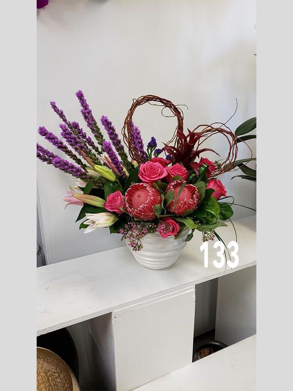 A vase filled with pink and purple flowers is sitting on a shelf.