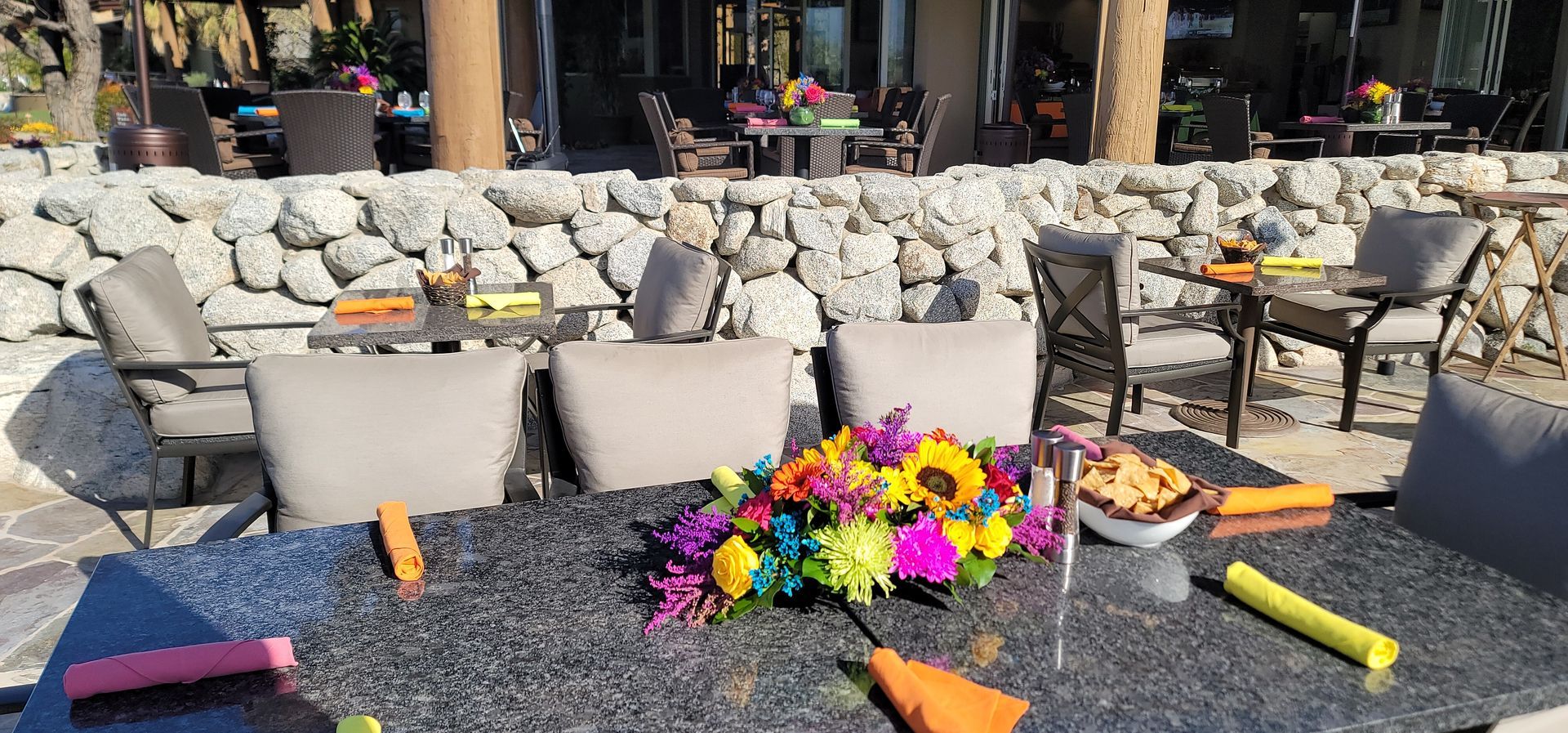 A table with a bunch of flowers on it in front of a stone wall.