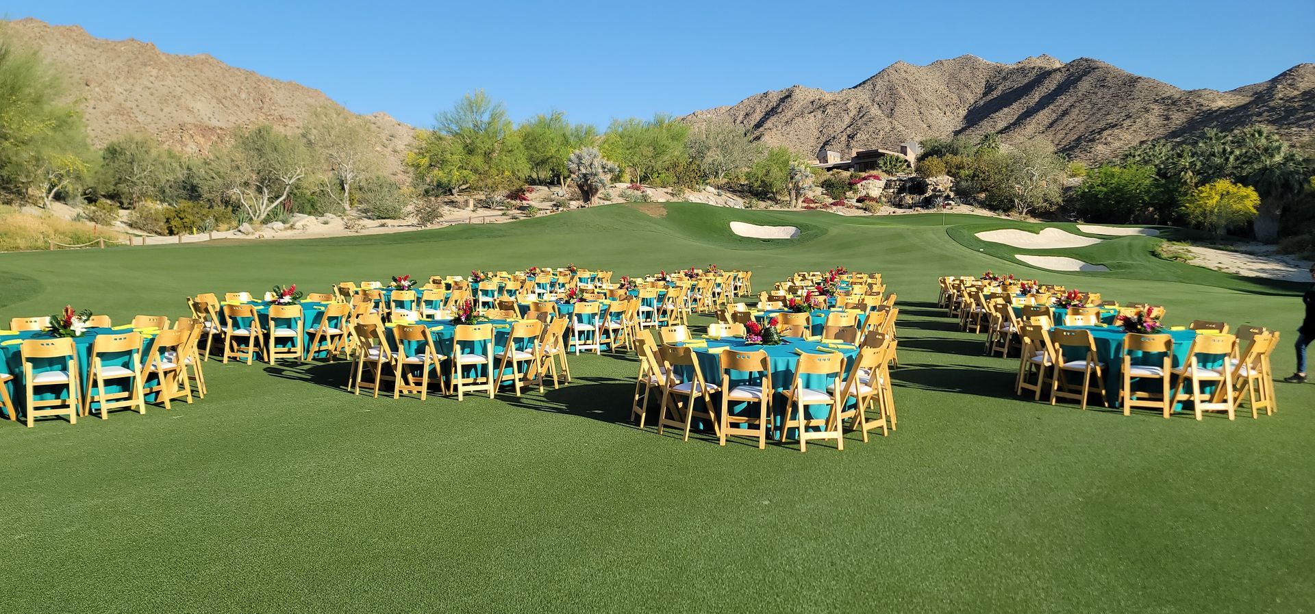 A row of tables and chairs are lined up on a lush green field.