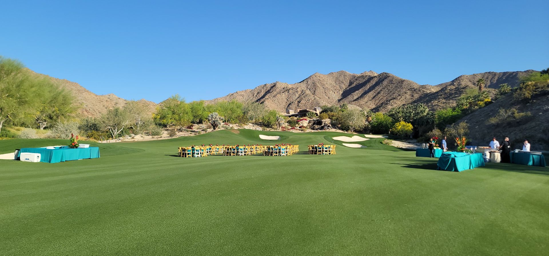 A group of people are standing on a golf course with mountains in the background.