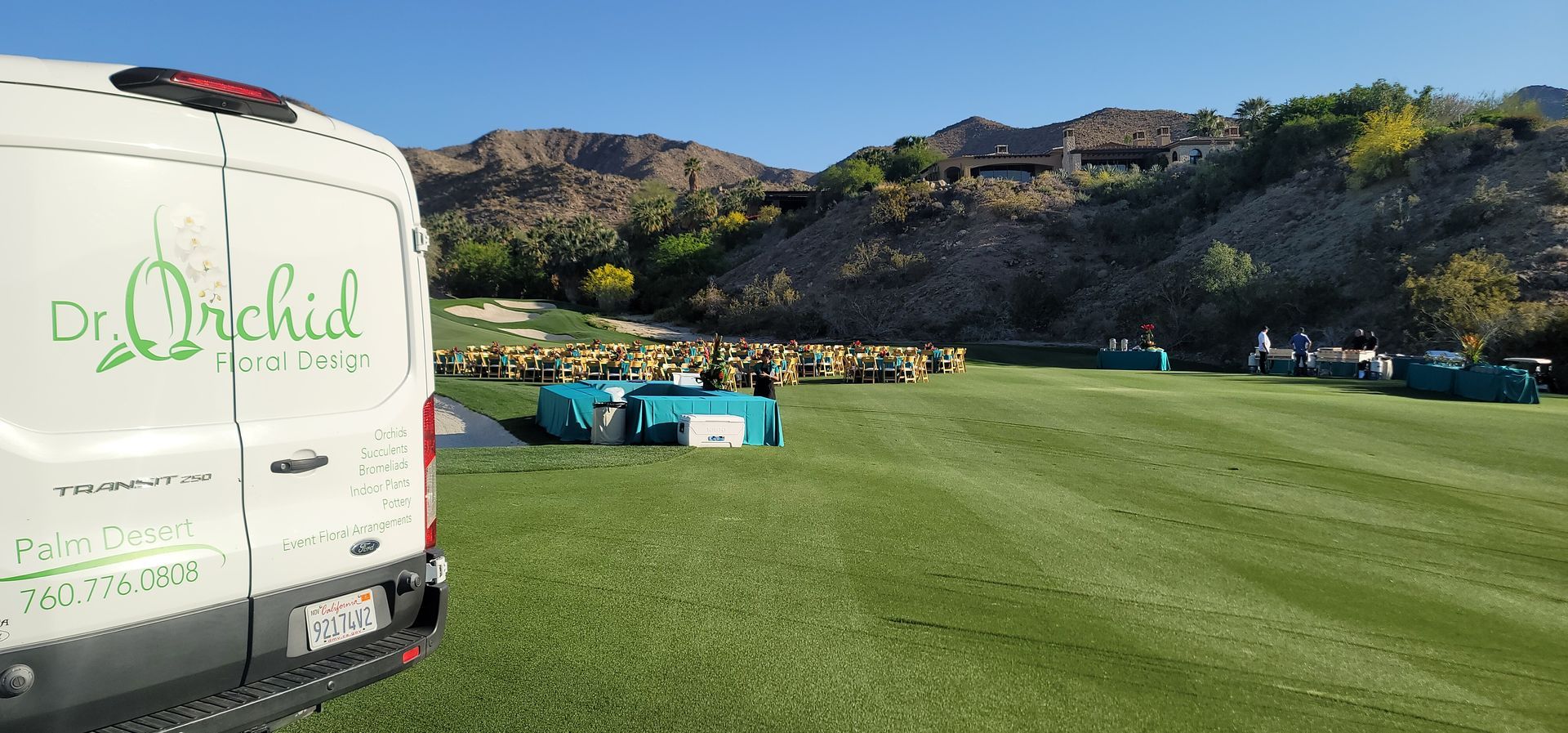 A white van is parked in a grassy field with mountains in the background.