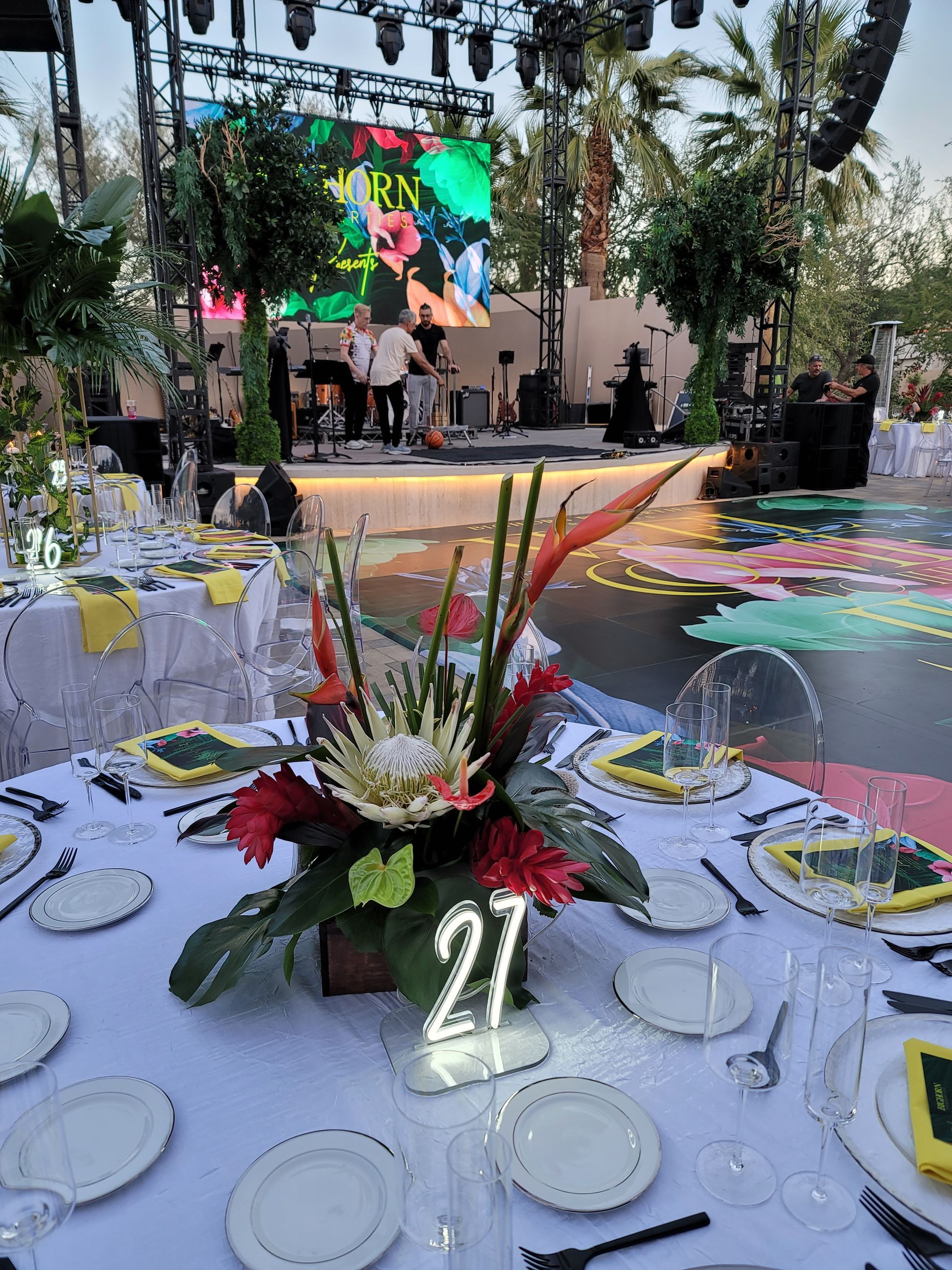 A table with plates , utensils , and a vase of flowers with the number 27 on it.