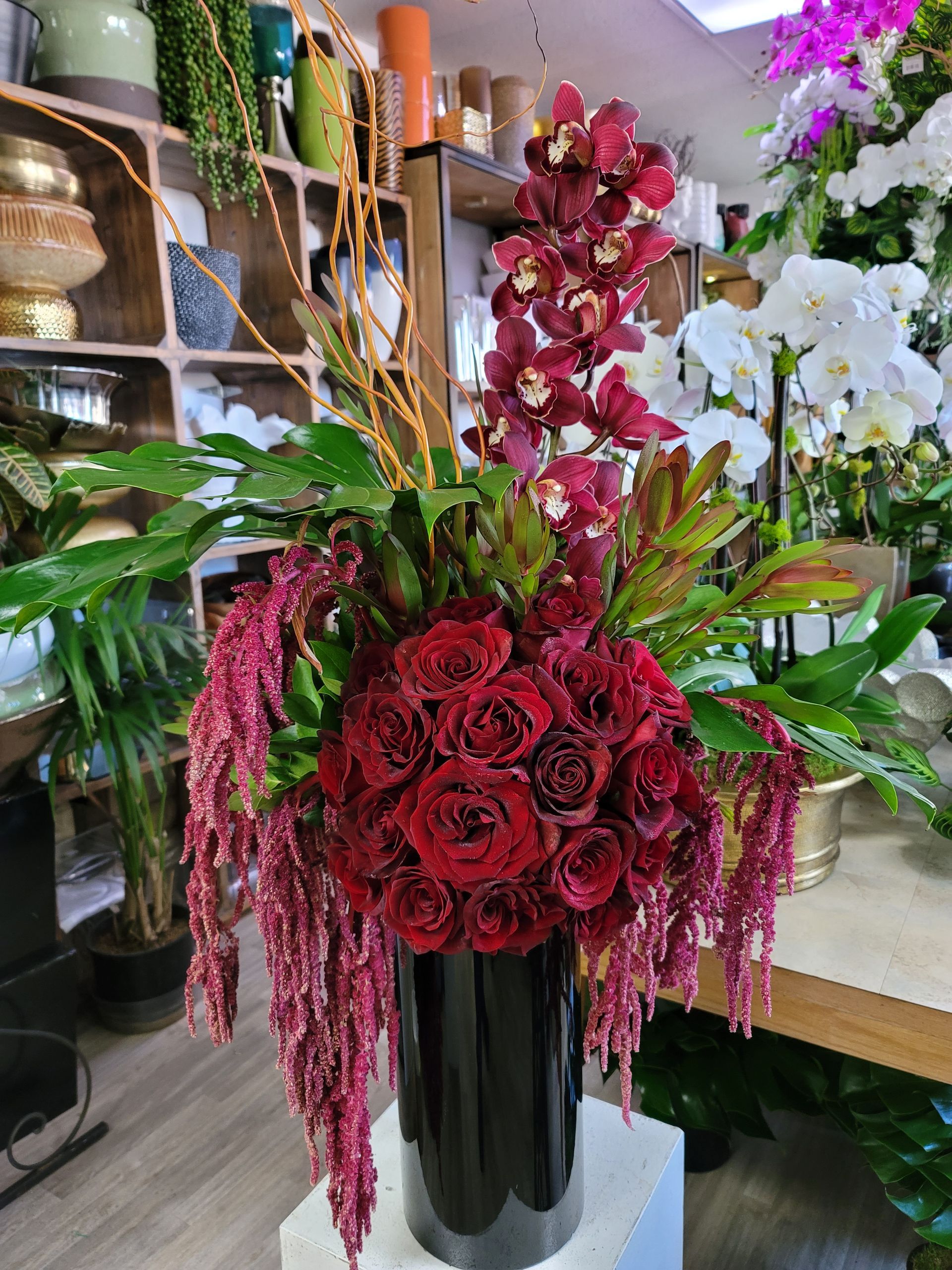 A vase filled with red roses and orchids is sitting on a table in a flower shop.