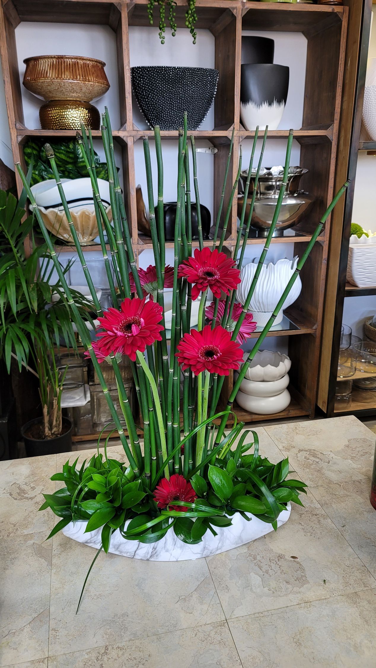 A vase filled with red flowers and greenery is sitting on a table.