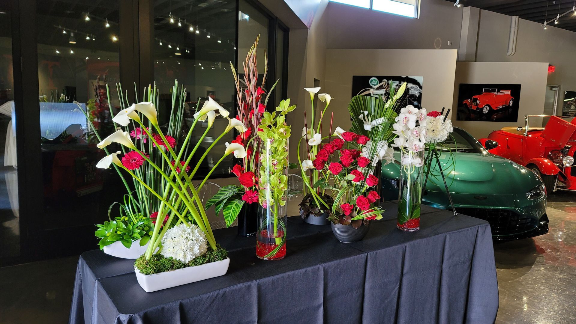 A table with vases of flowers and a green car in the background