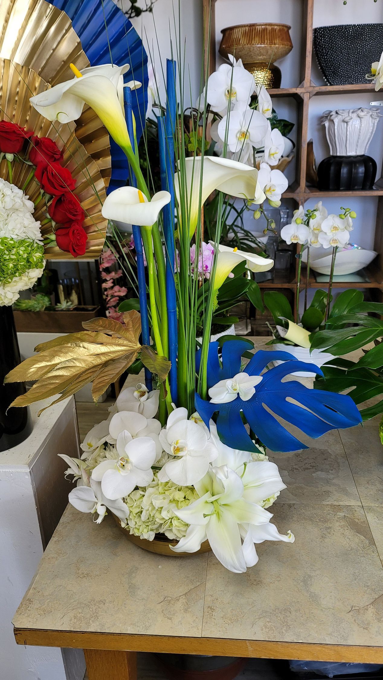 A vase filled with white flowers and blue leaves is on a table.