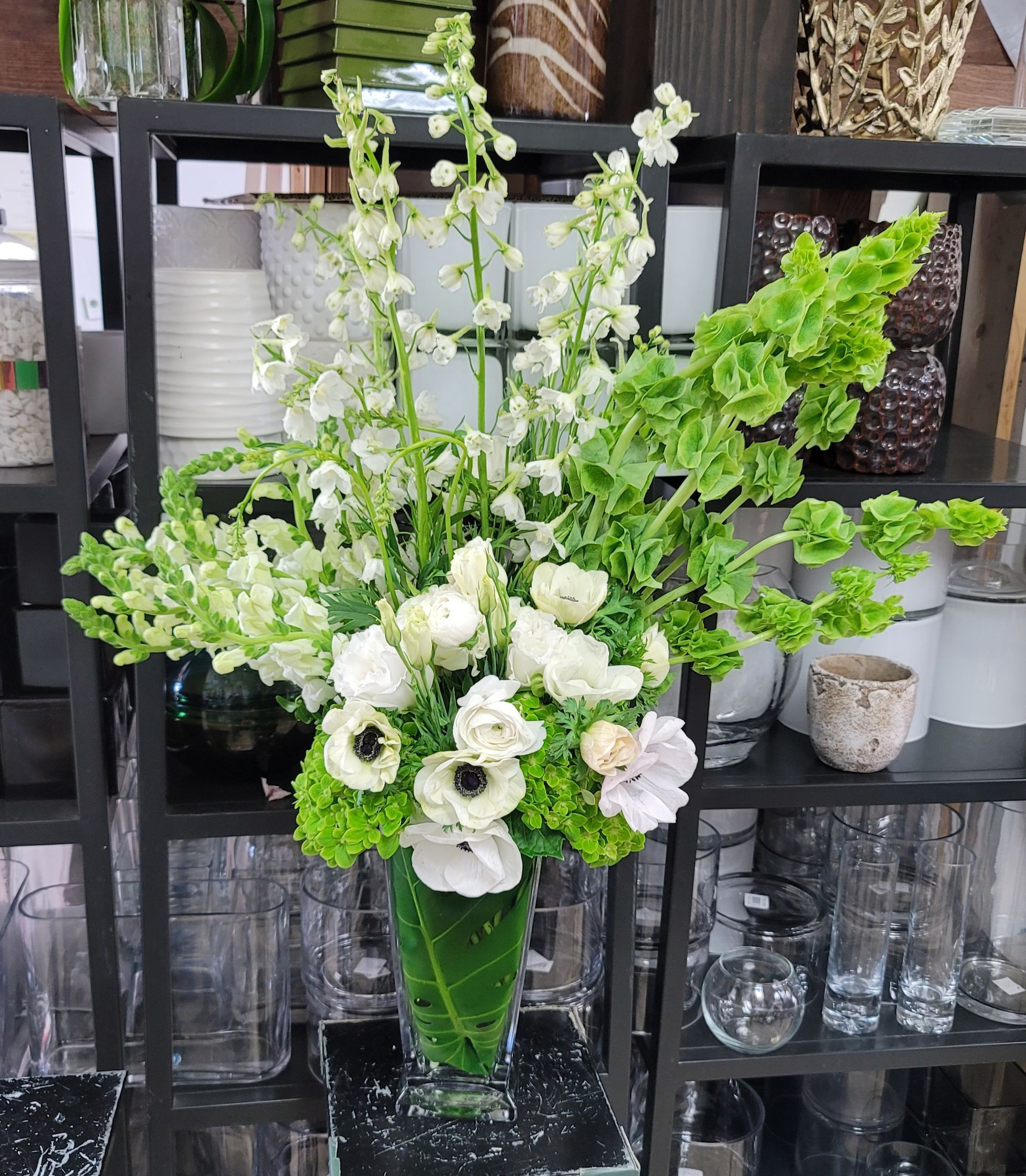 A vase filled with white flowers and greenery is sitting on a table.