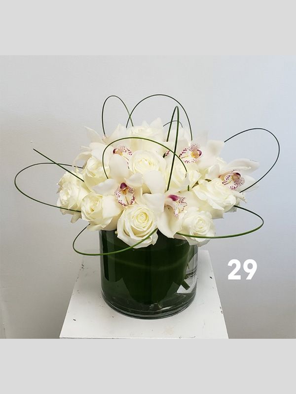 A vase filled with white roses and orchids on a table.