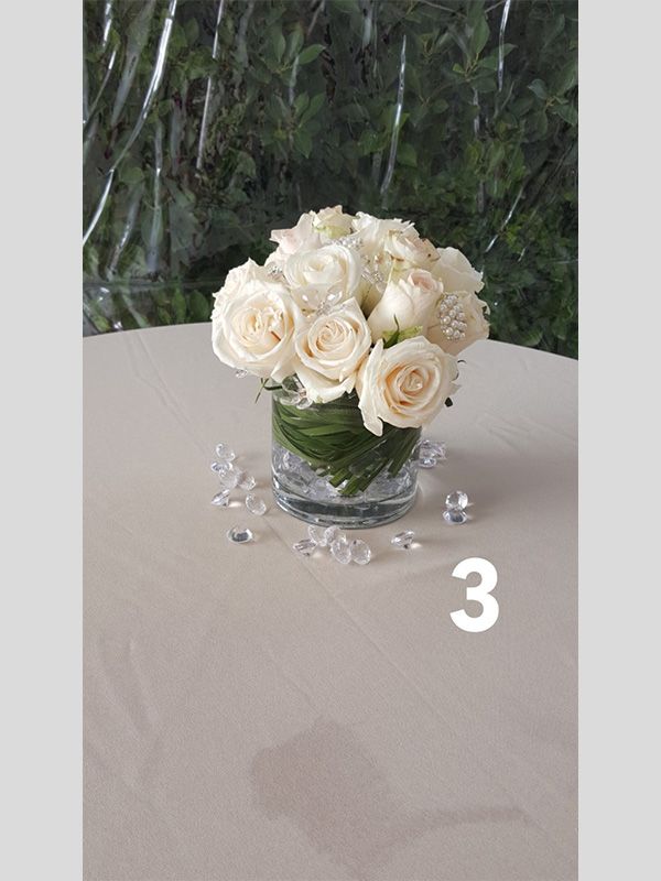A vase of white roses sits on a table next to the number 3