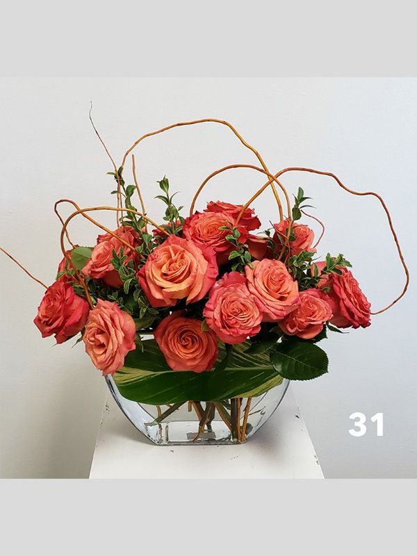 A vase filled with red roses and green leaves