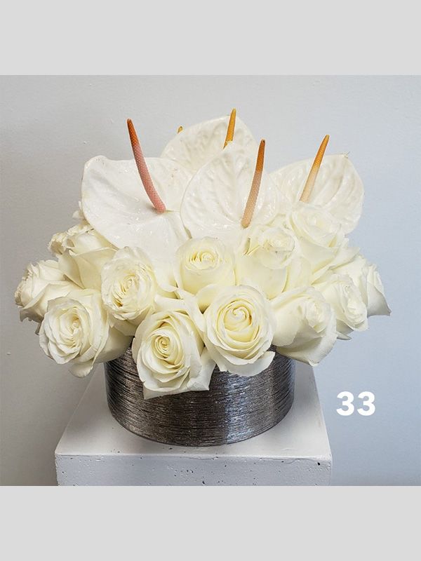 A vase filled with white roses and anthuriums