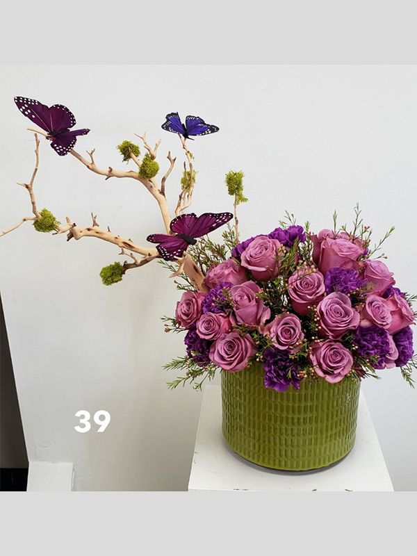 A vase filled with purple roses and butterflies on a table.