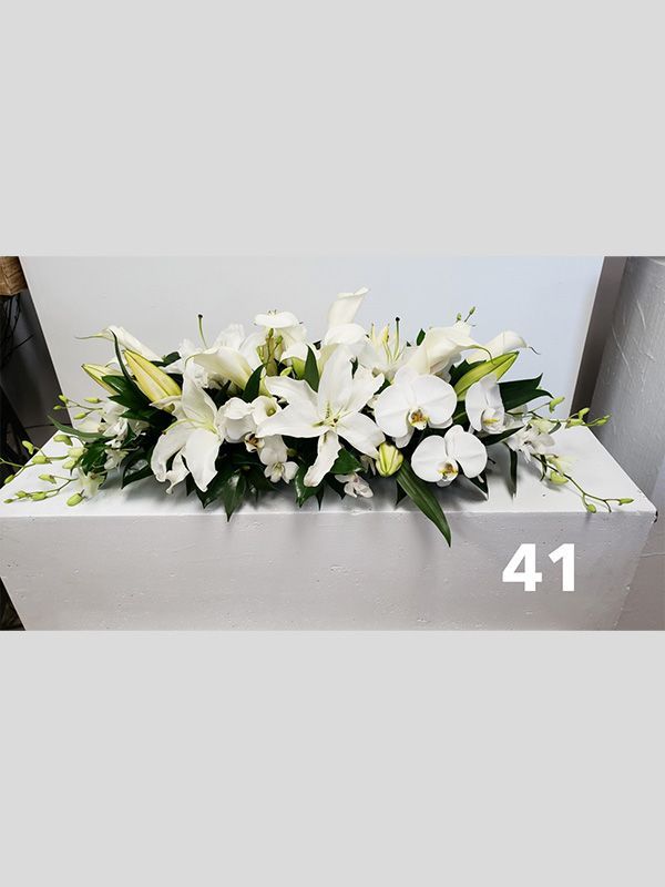 A long bouquet of white flowers is sitting on top of a white table.