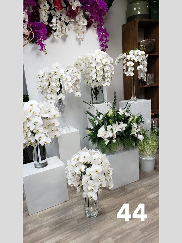 A bunch of white flowers in vases are sitting on a wooden floor.