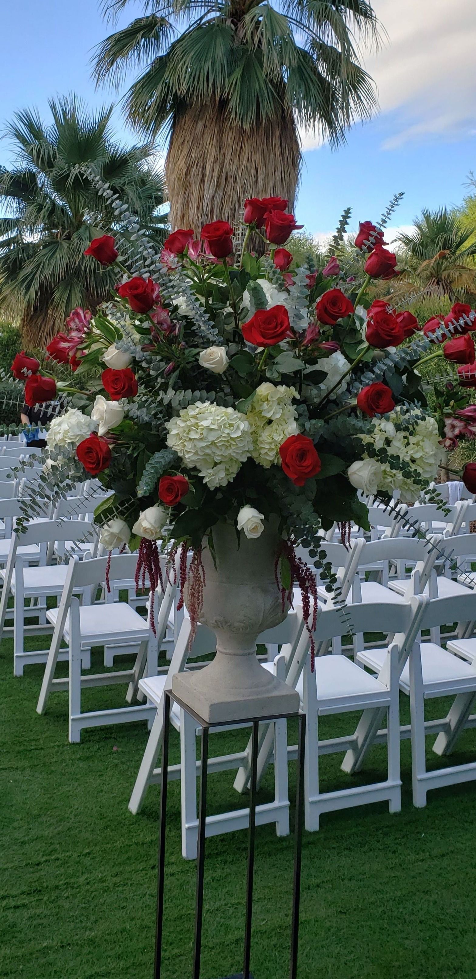A large vase filled with red and white flowers is sitting in front of a row of white chairs.