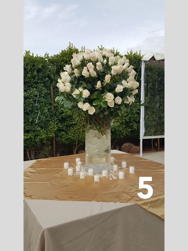A table with a vase of white roses and candles on it