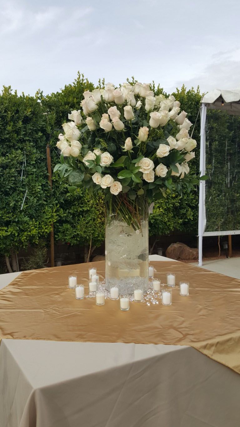 A table with a vase of white roses and candles on it.
