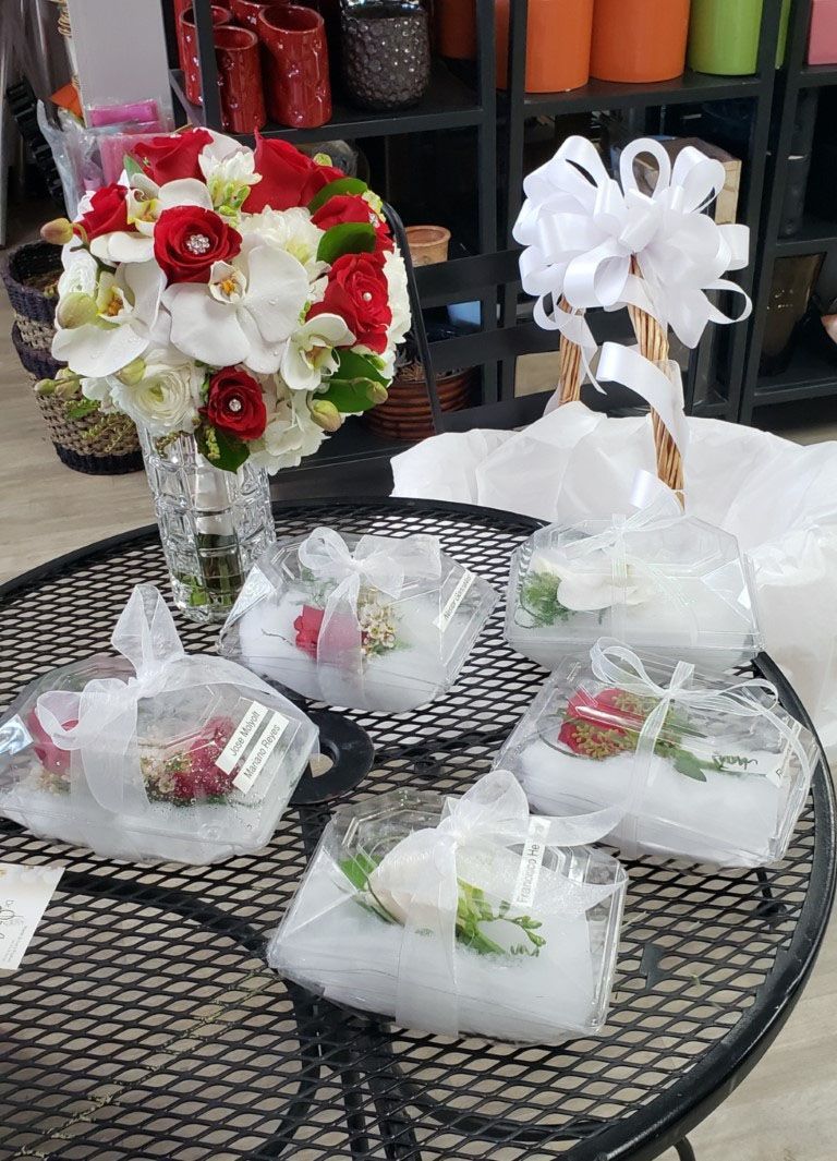 A table with a vase of flowers and a bunch of flowers in plastic containers.