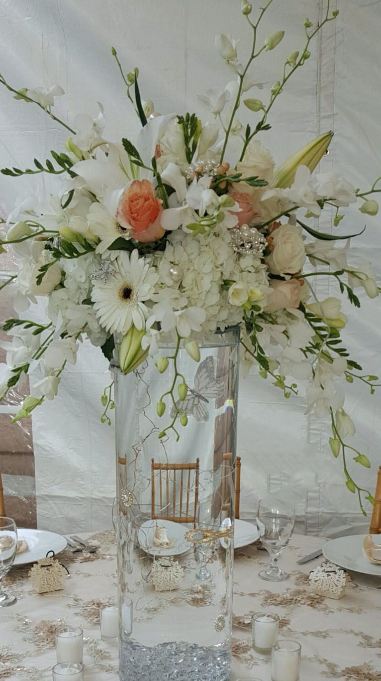 A tall vase filled with white flowers is on a table.