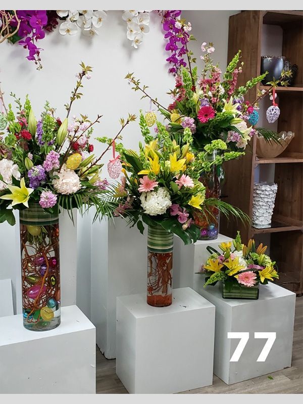 Three vases filled with flowers are sitting on white blocks with the number 77 on them.