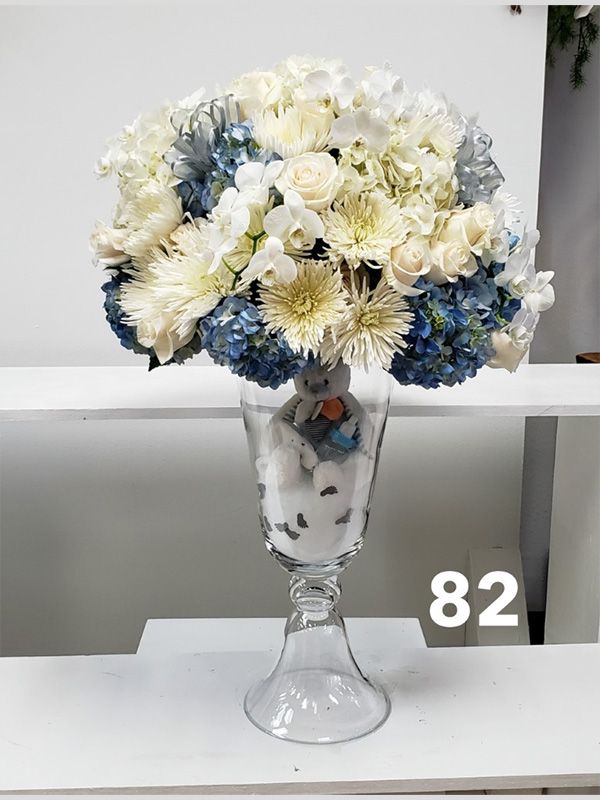 A vase filled with blue and white flowers and a teddy bear.