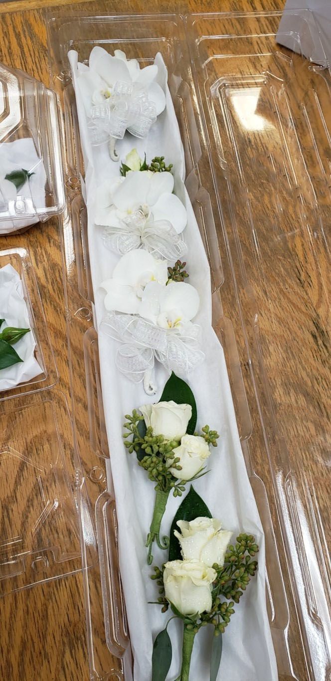 A row of white roses in a plastic container on a wooden table.