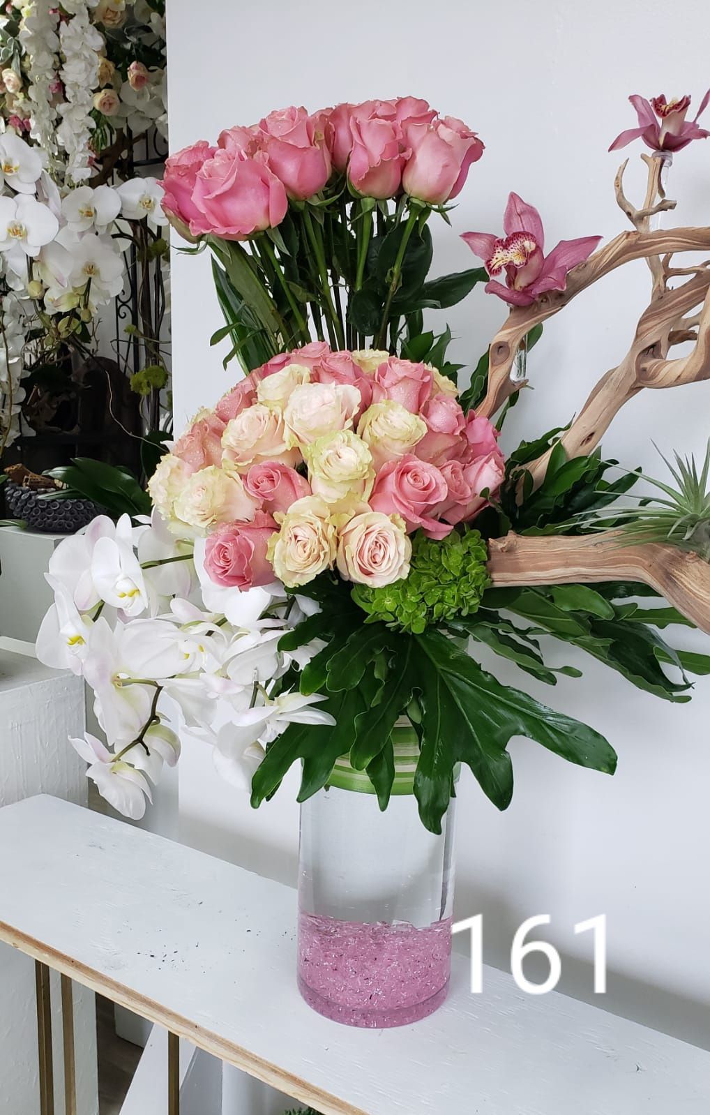 A vase filled with pink roses and orchids is sitting on a table.