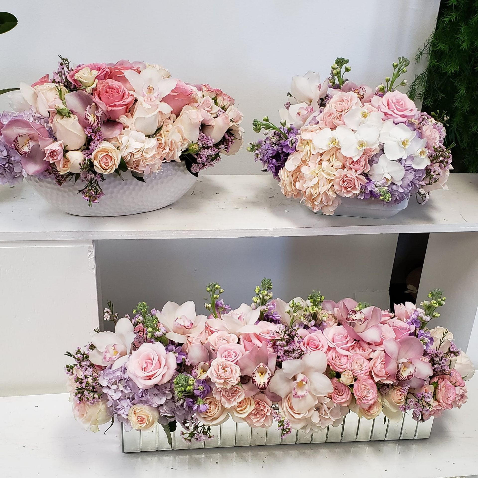 Three vases filled with pink and purple flowers are on a shelf.