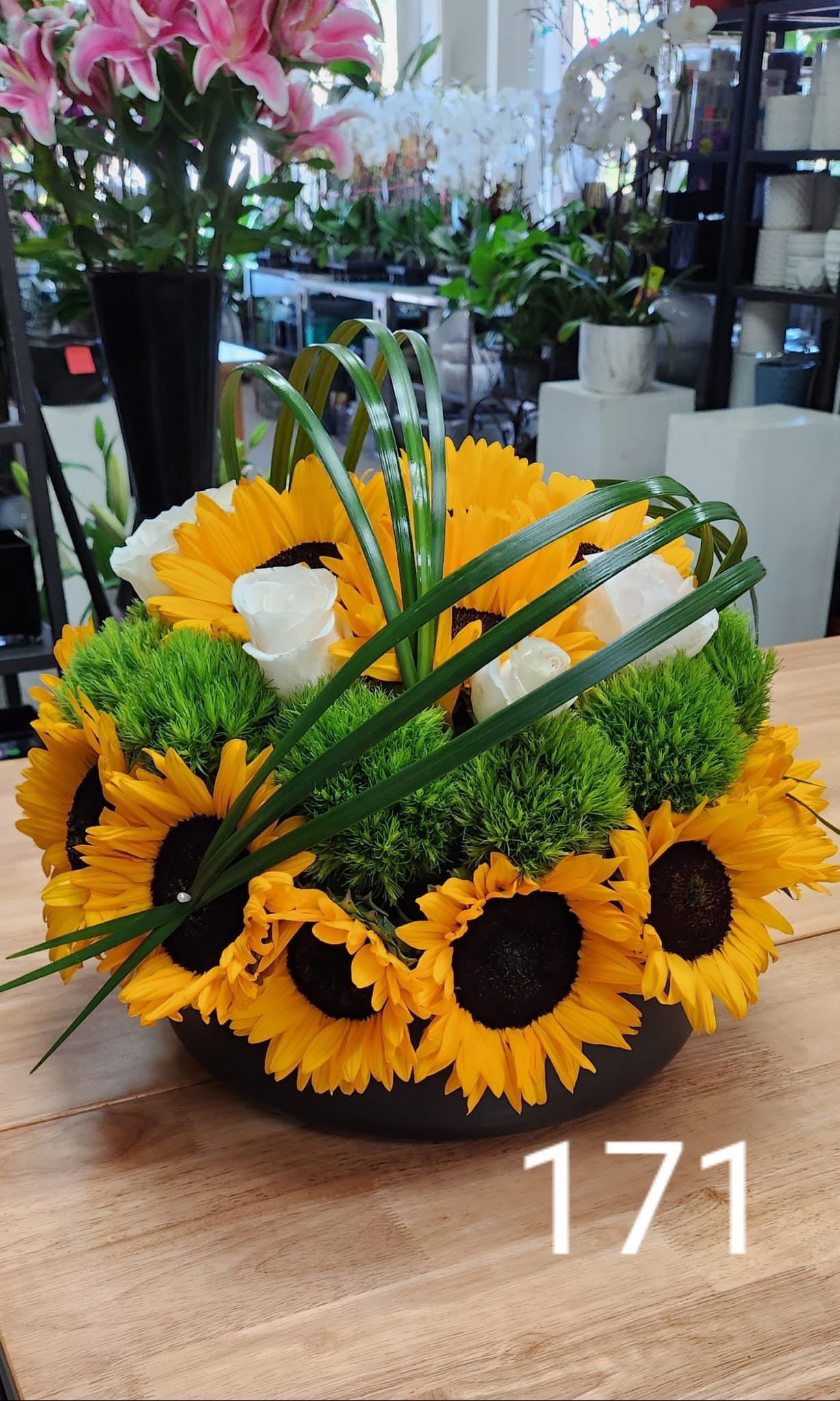 A vase filled with sunflowers and greenery is sitting on a wooden table.