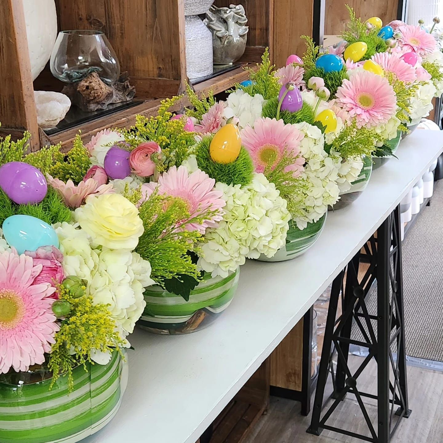A row of vases filled with flowers and easter eggs on a table.