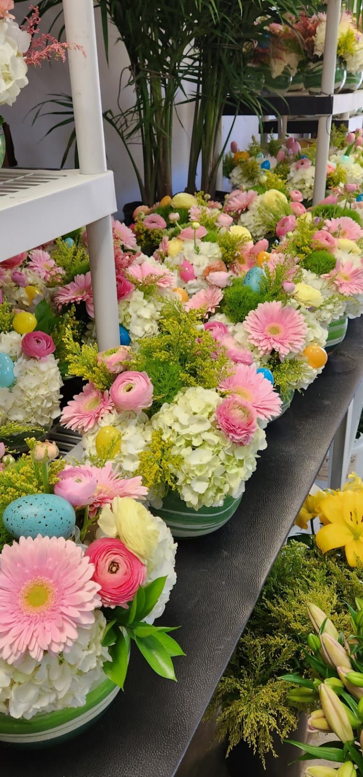 A row of vases filled with flowers and easter eggs on a table.