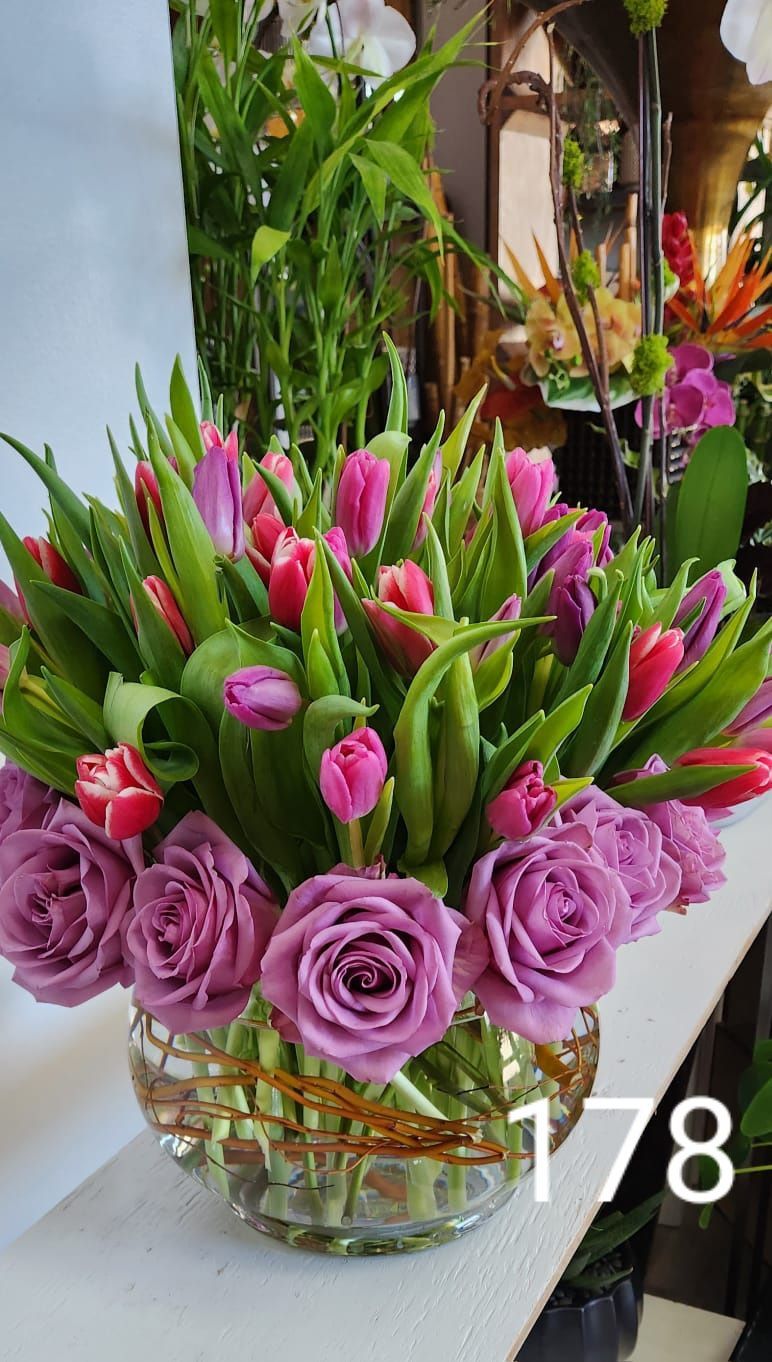 A vase filled with purple roses and pink tulips is sitting on a table.