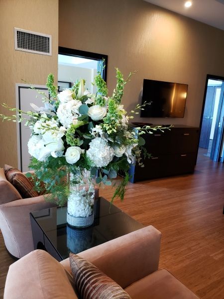 A vase filled with white flowers is on a table in a living room.