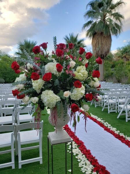 A large vase filled with red and white flowers is sitting on a table in front of a row of white chairs.