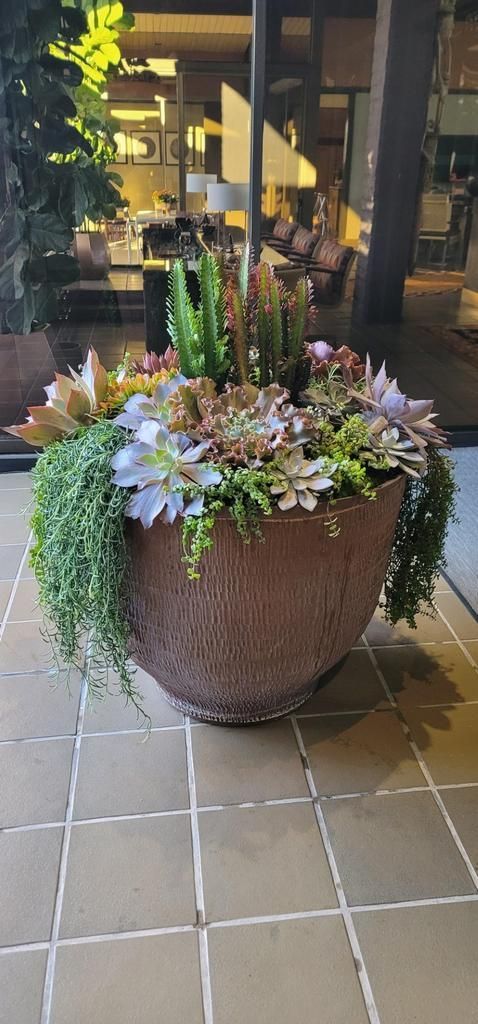 A large pot filled with flowers and plants is sitting on a tiled floor.