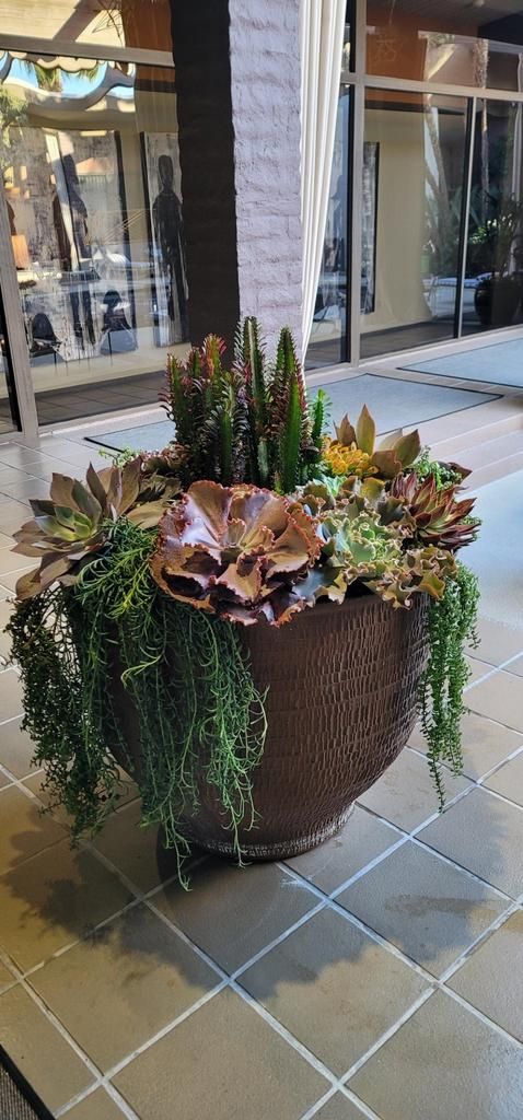 A large pot filled with lots of plants is sitting on a tiled floor.