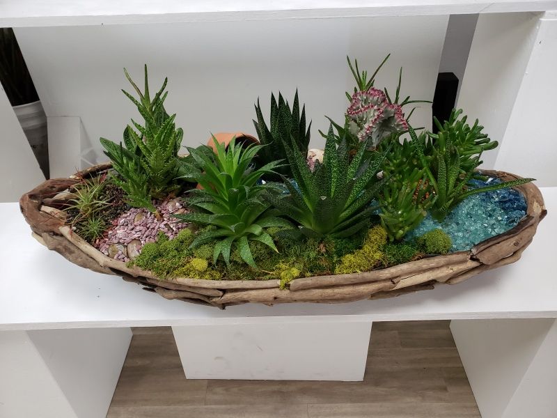 A wooden bowl filled with plants is sitting on a shelf.