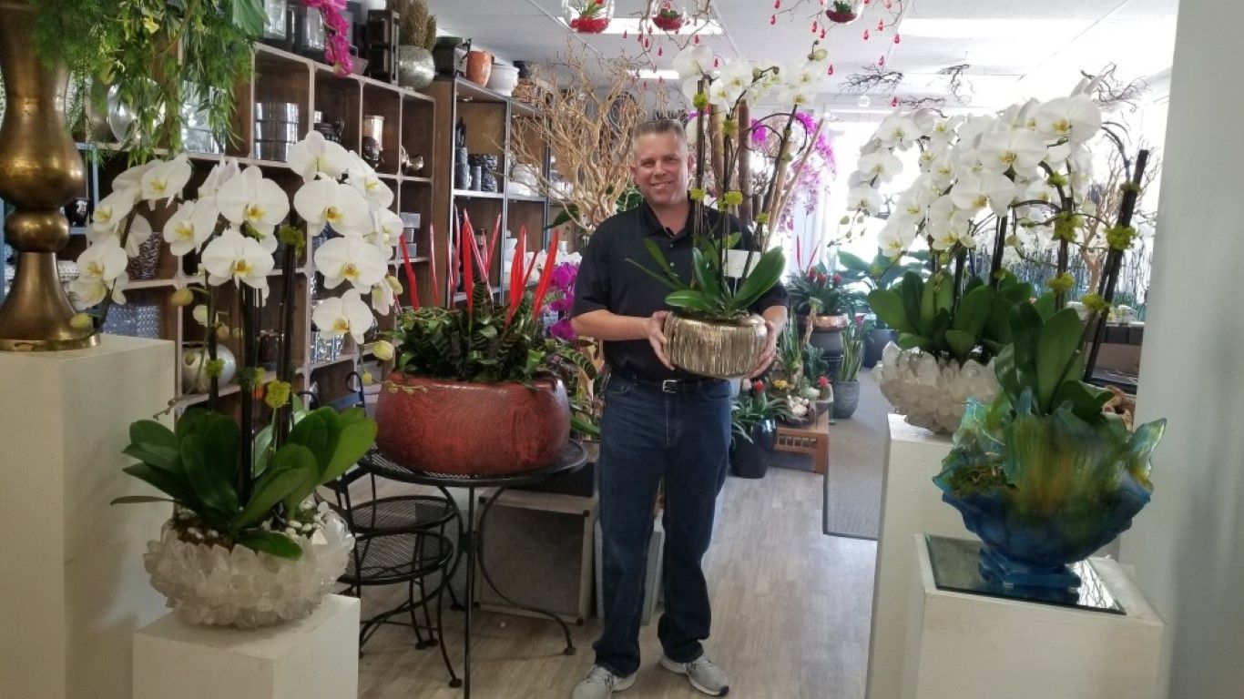 A man is holding a potted plant in a flower shop.
