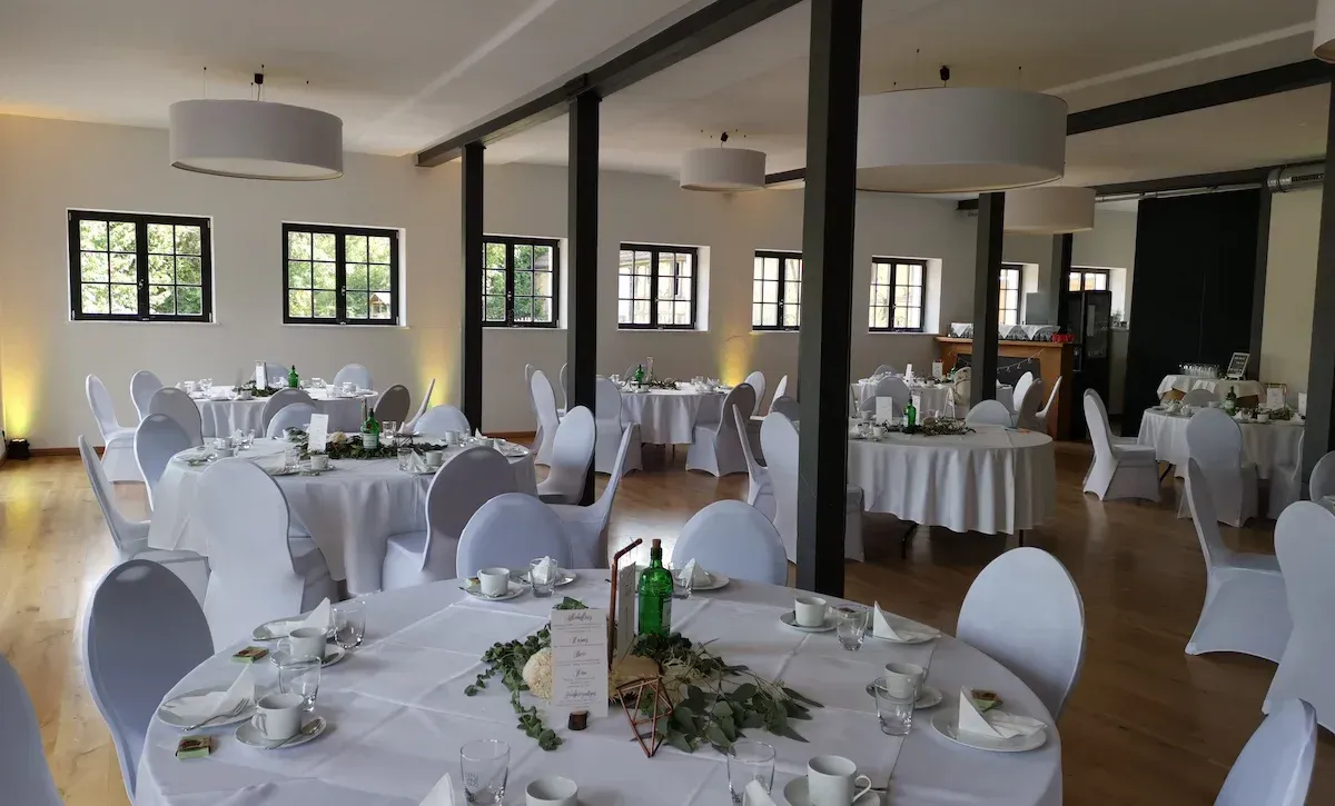 Paulinenhof Kuhlowitz bei Bad Belzig – heller Hochzeitssaal mit runden Tischen, großen Fenstern und modernem Lichtambiente in Brandenburg