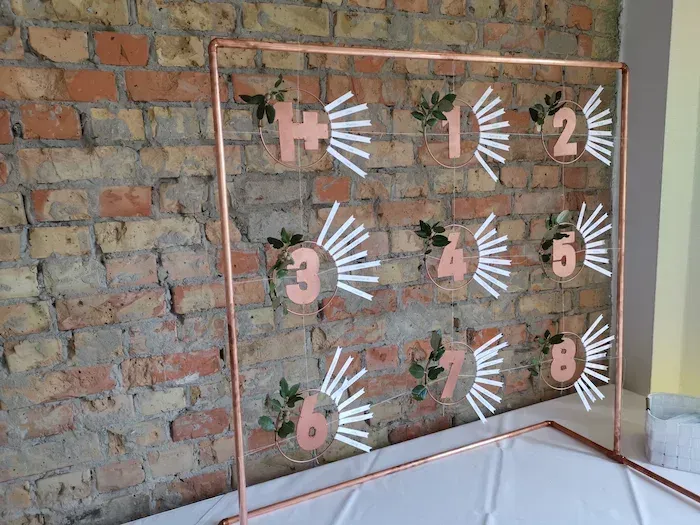 Paulinenhof Kuhlowitz (Brandenburg) – moderner Sitzplan als Kupferrahmen vor Ziegelwand, stilvolle Hochzeitsdeko bei Bad Belzig