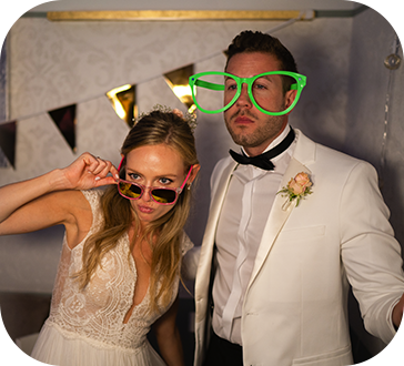 A bride and groom wearing sunglasses and green glasses pose for a picture.