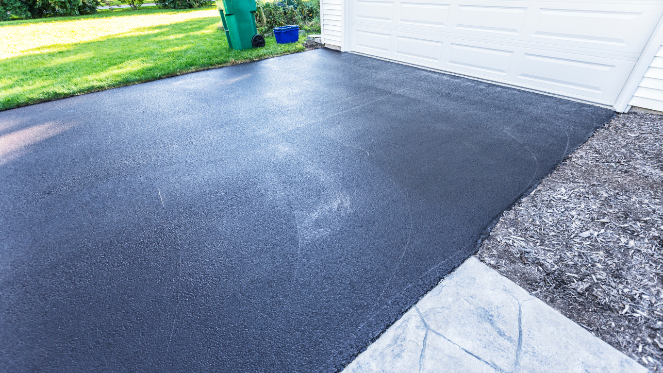 A blacktop driveway next to a white garage door.