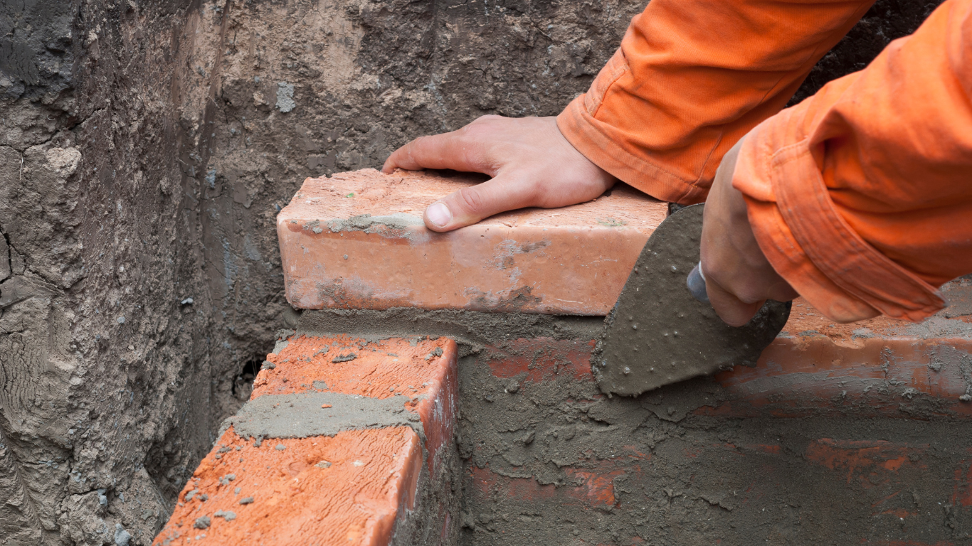 A person is laying bricks on the ground with a trowel.