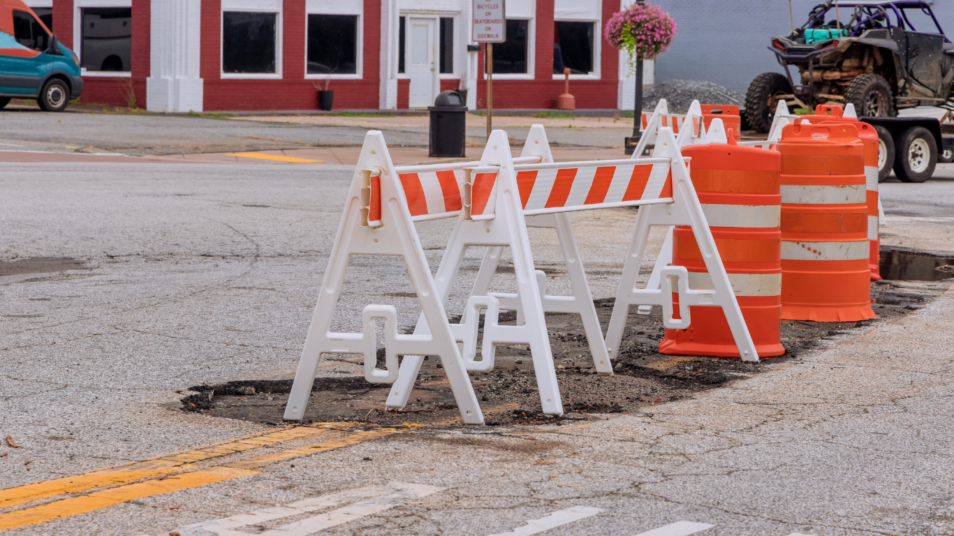 A row of orange and white construction barriers on the side of a road for asphalt repair.